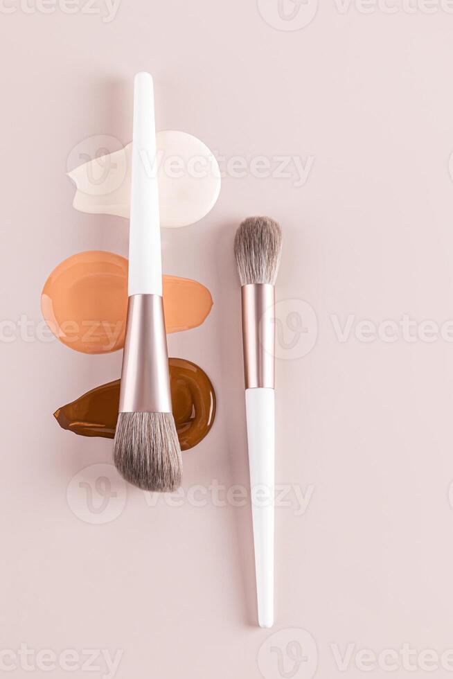 A beautiful cosmetic background with texture samples of liquid foundation powder in different tones and two makeup brushes. vertical top view. layout. photo