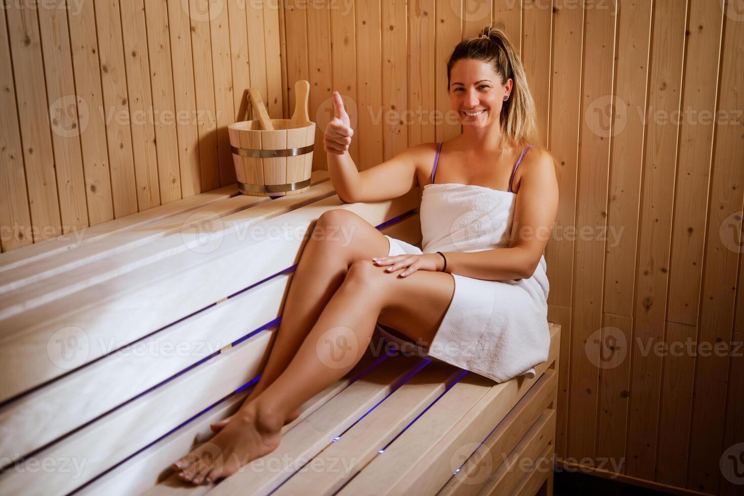 Happy woman enjoys a private sauna at a high-end spa. She is looking at camera, smiling and showing thumbs up. photo