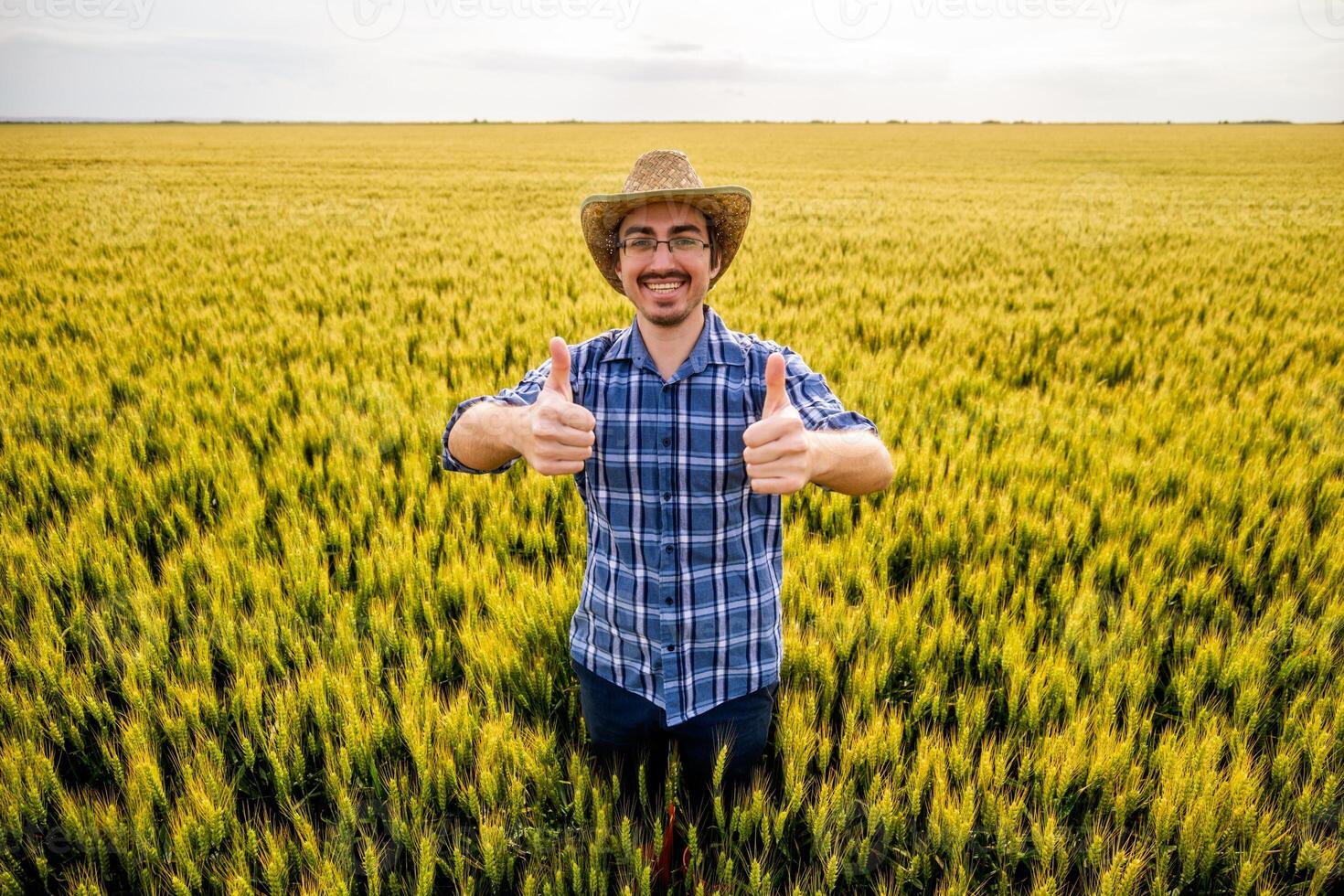 Happy farmer standing in his wheat field. Portrait of agricultural worker in the growing wheat field. photo