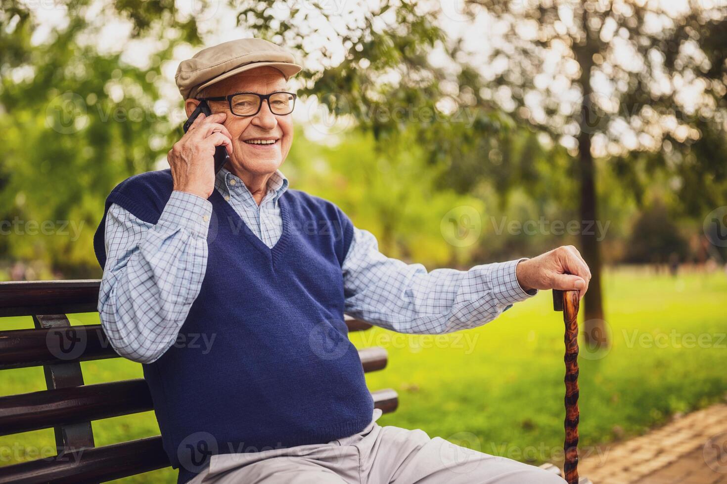 Cheerful senior man sitting on bench in park and talking on mobile phone. photo