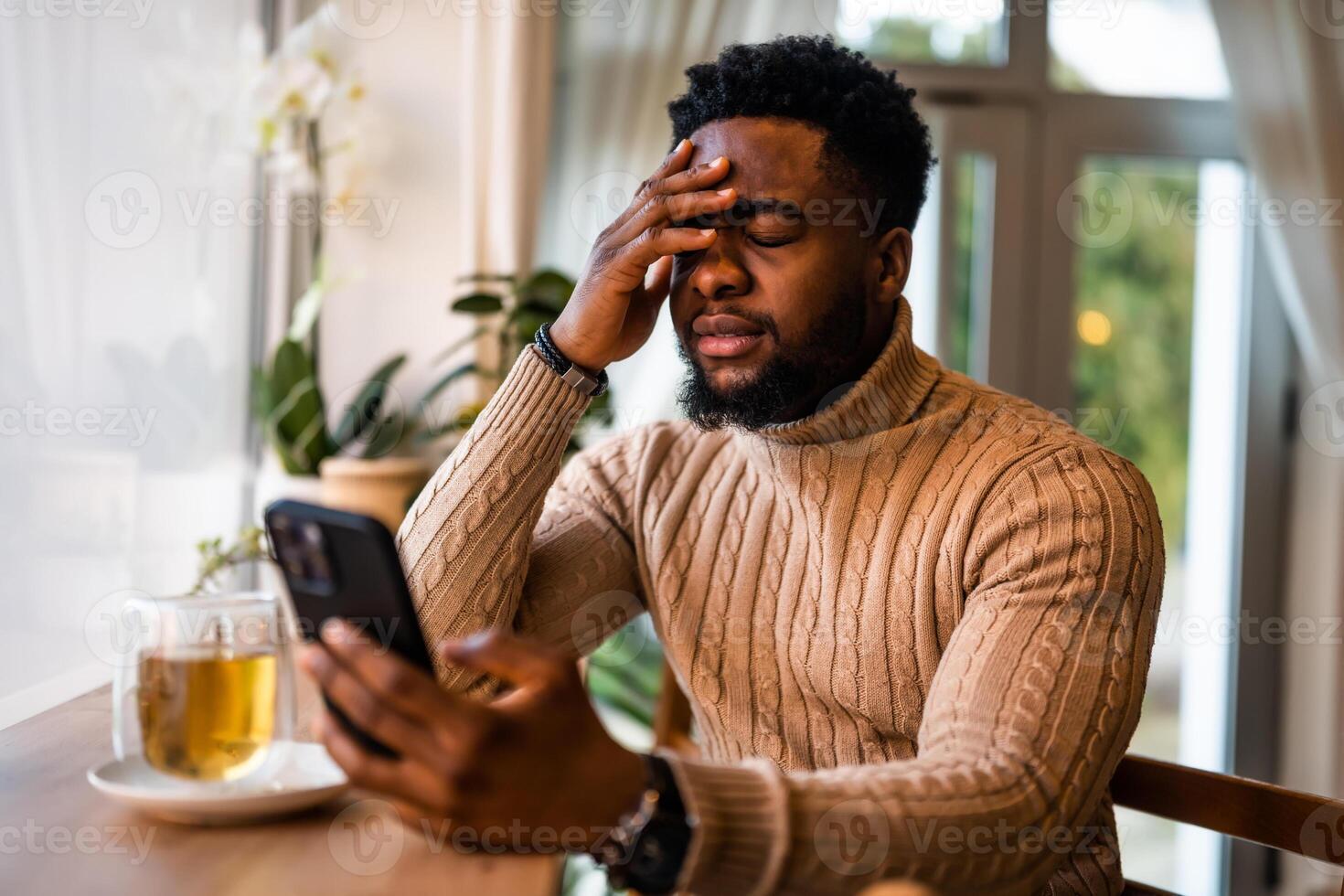 A young black man sits at the bar, using smartphone, messaging online. He is anxious and preoccupied. photo