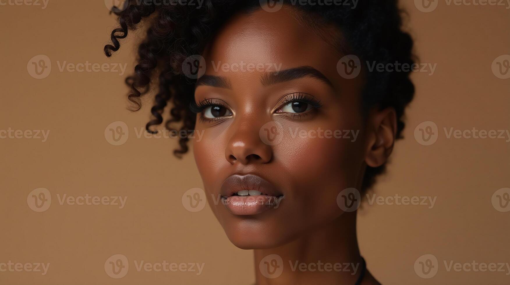 A person with curly hair stands in a neutral brown setting. photo