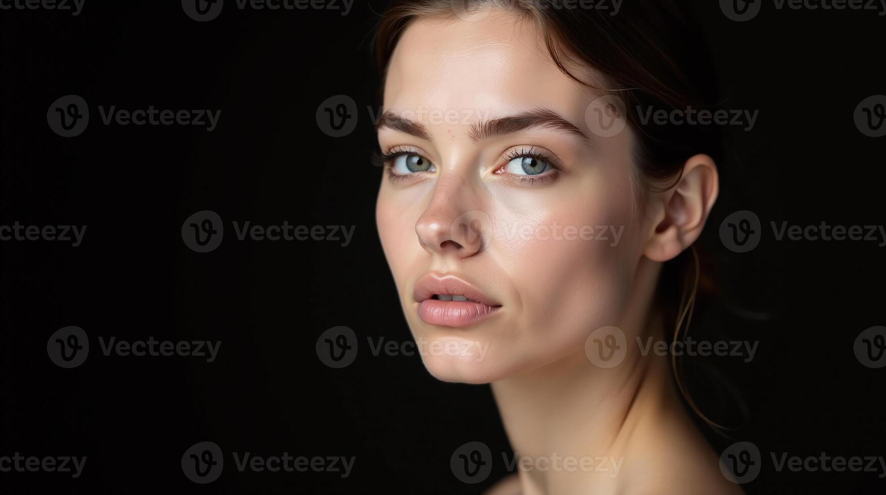 A woman with a serene expression, her face illuminated subtly against a dark background. photo