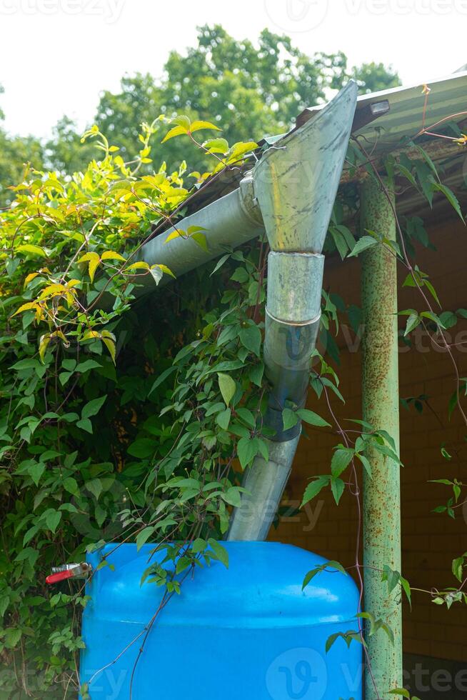Water collection tank under a roof with a drain in garden. Rain water harvesting architecture. photo