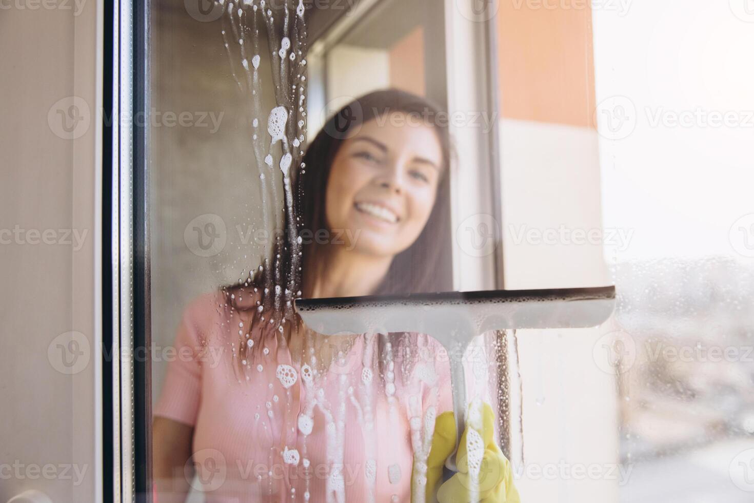Smiling woman cleaning a window with a squeegee photo