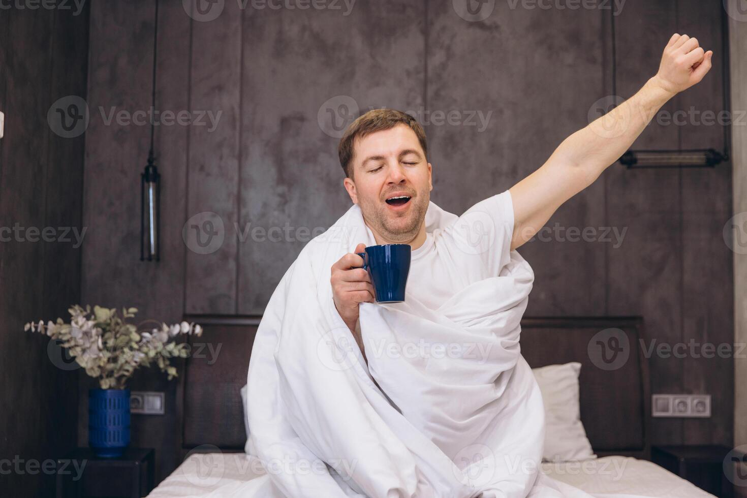 Man Waking Up and Stretching in Bed While Drinking Coffee photo
