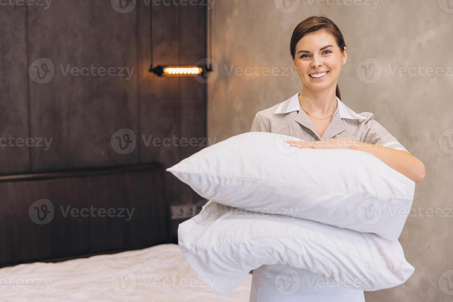 Chambermaid holding clean pillows smiling in hotel room photo