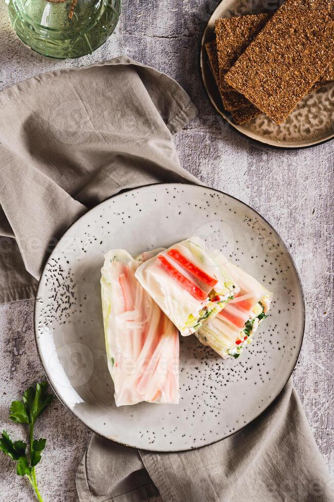 Spring rolls with crab meat, cucumber and herbs on a plate on the table top and vertical view photo