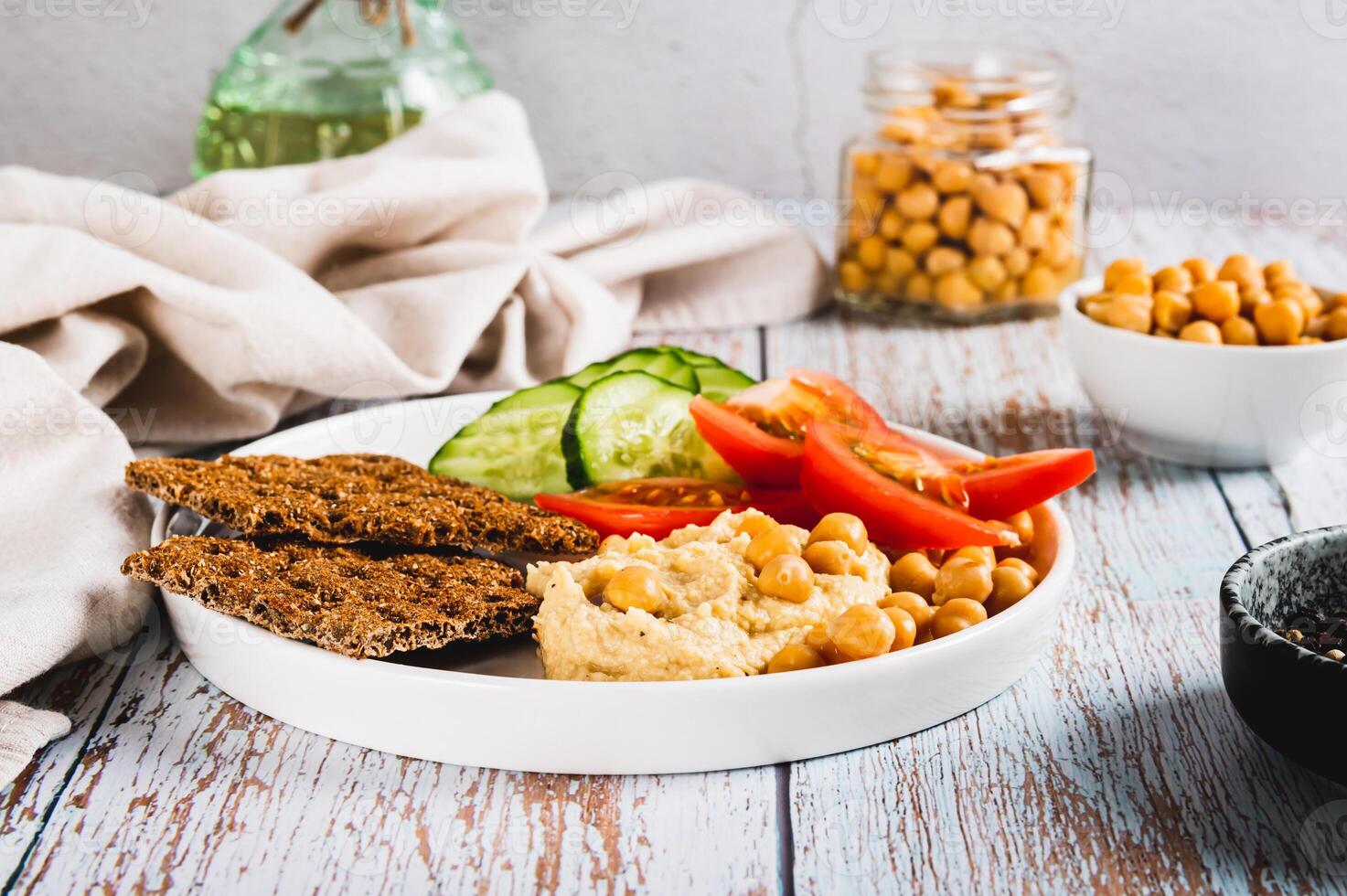 Hummus, chickpeas, tomato, cucumber, grain crackers on a plate on the table photo