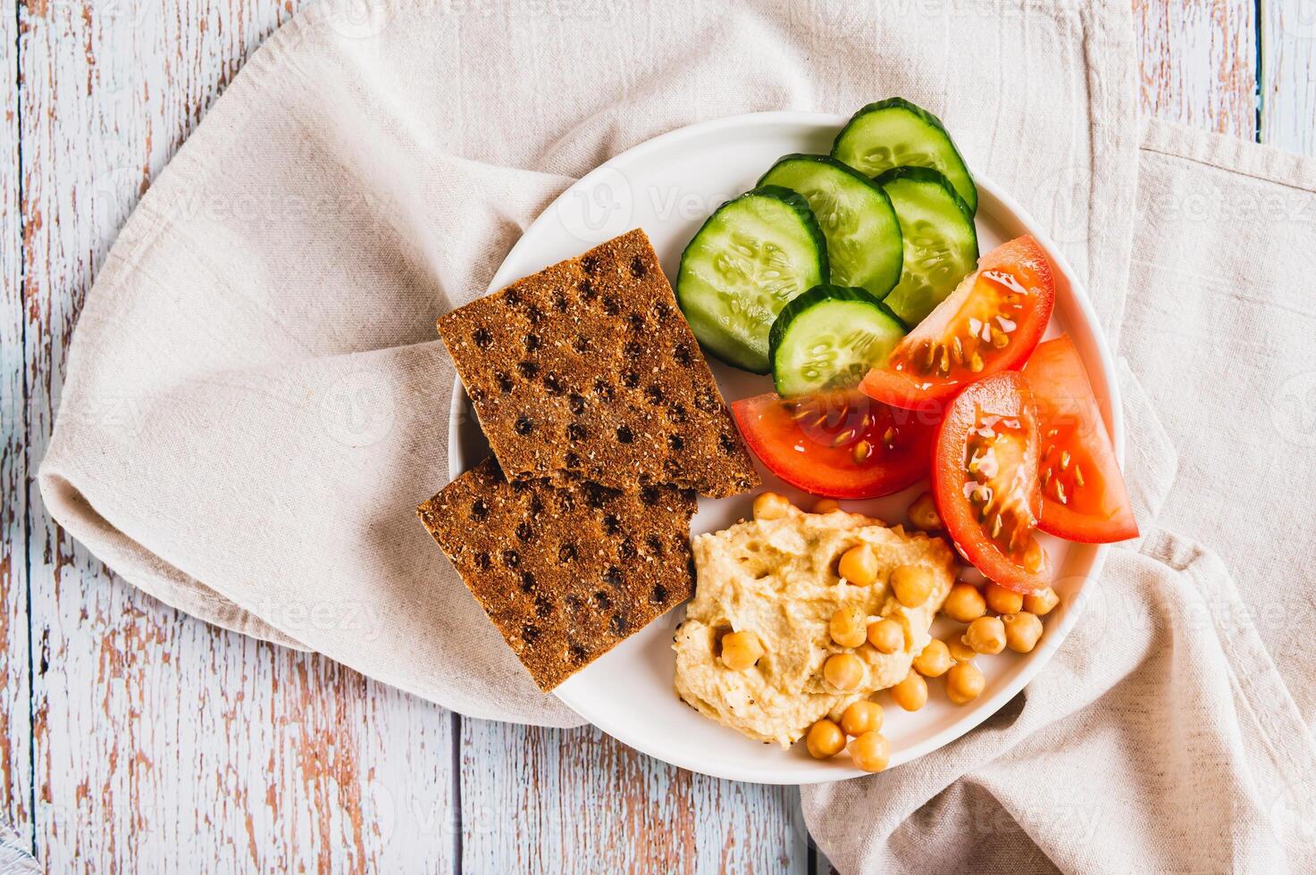 Close up of platte with hummus, chickpeas, tomato, cucumber and grain crackers on a plate top view photo