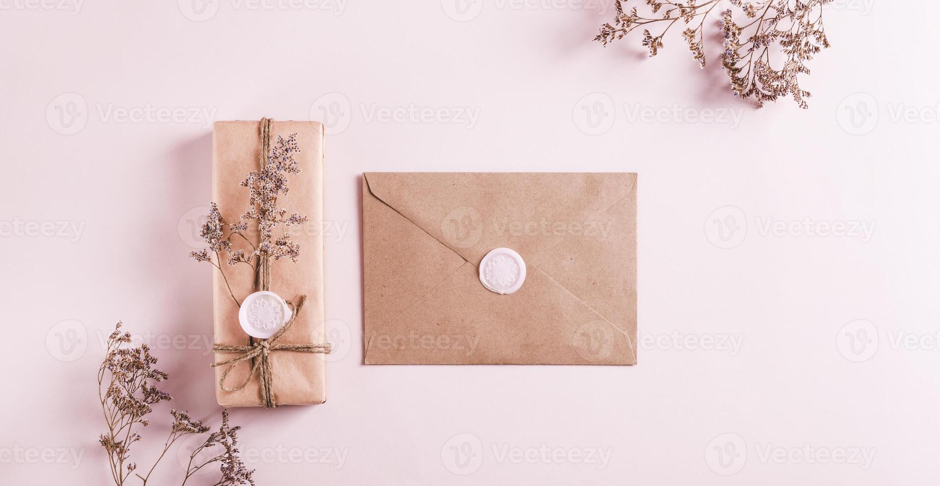Gift in kraft paper and envelope with wax seals and dried flowers on pink top view web banner photo