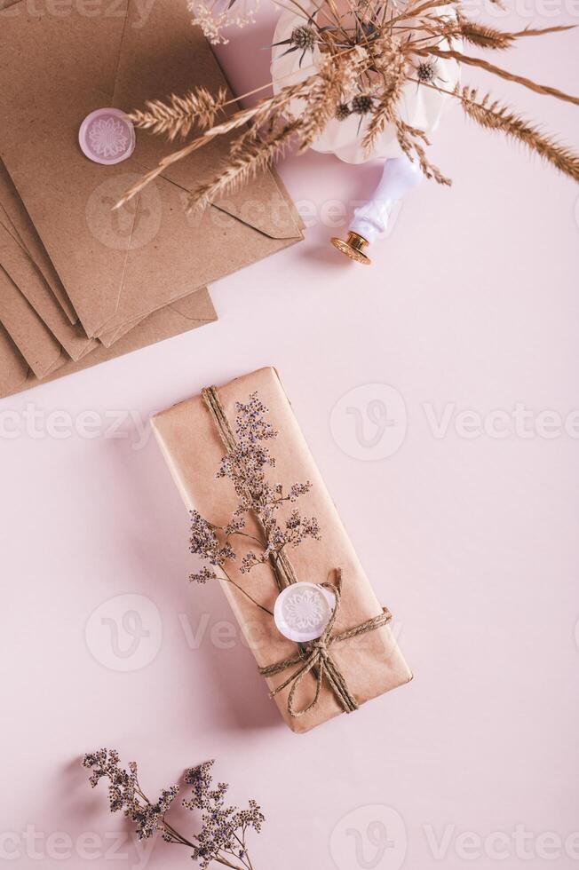 Gift in craft paper with wax seal and dried flowers on pink top and vertical view photo