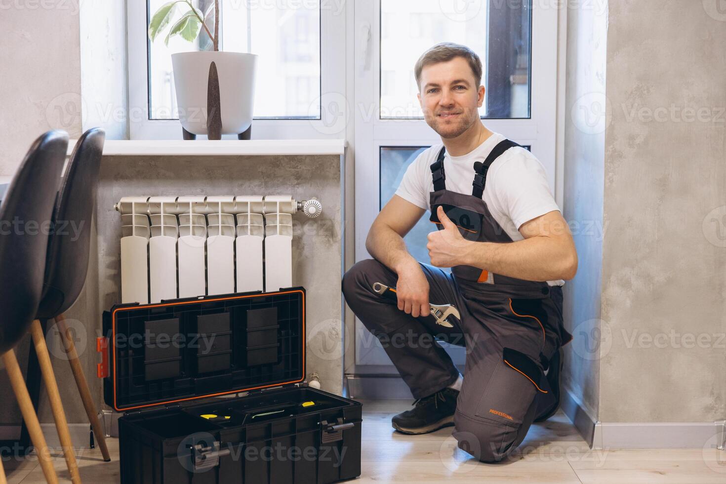 Plumber showing thumbs up near radiator and toolbox photo