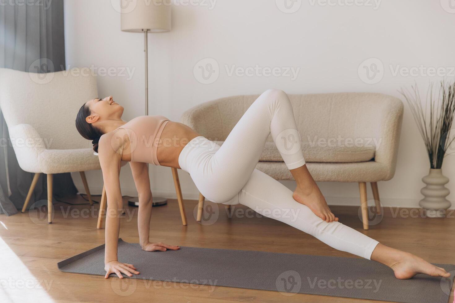 Young woman practicing reverse table top pose on yoga mat at home photo