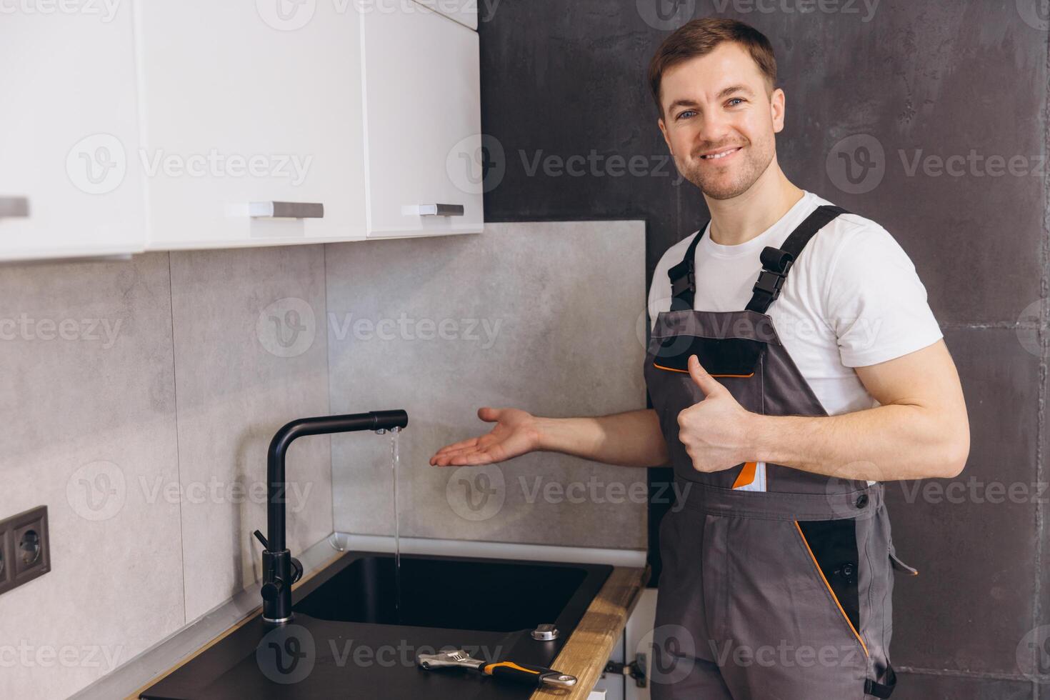 Plumber showing running water from tap after successful installation in kitchen photo