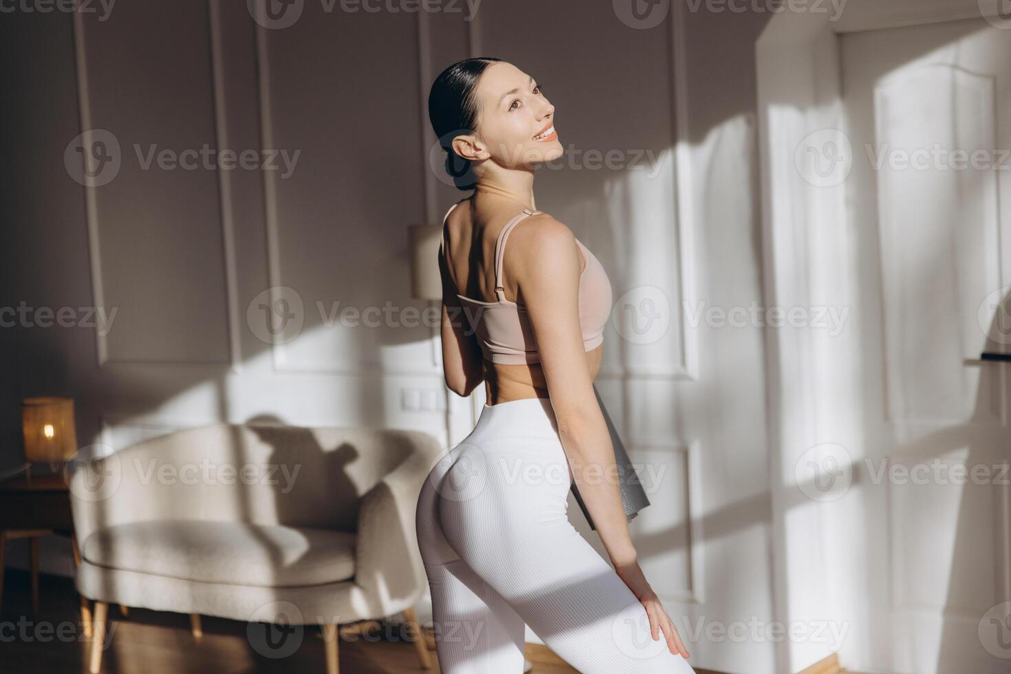 Young woman holding yoga mat and smiling in her living room photo
