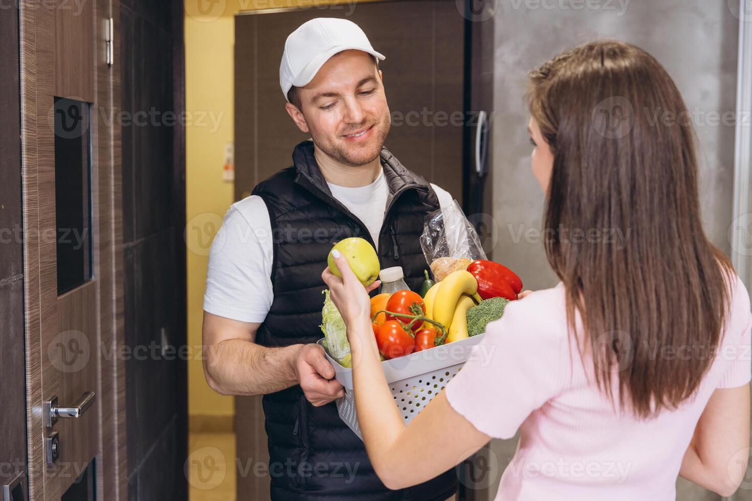 Delivery man handing fresh groceries to young woman at home photo