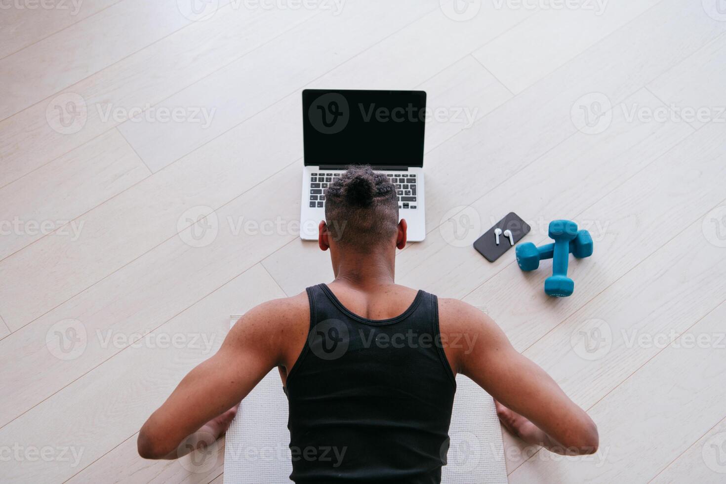 Training At Home. Sporty man doing the training while watching an online tutorial on a laptop, exercising in the living room, free space. photo