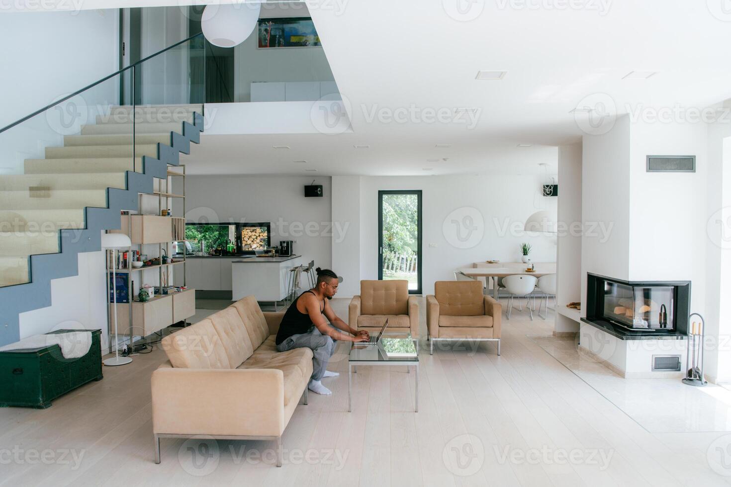 African American man in glasses sitting at a table in a modern living room, using a laptop for business chat, conversation with friends and entertainment photo