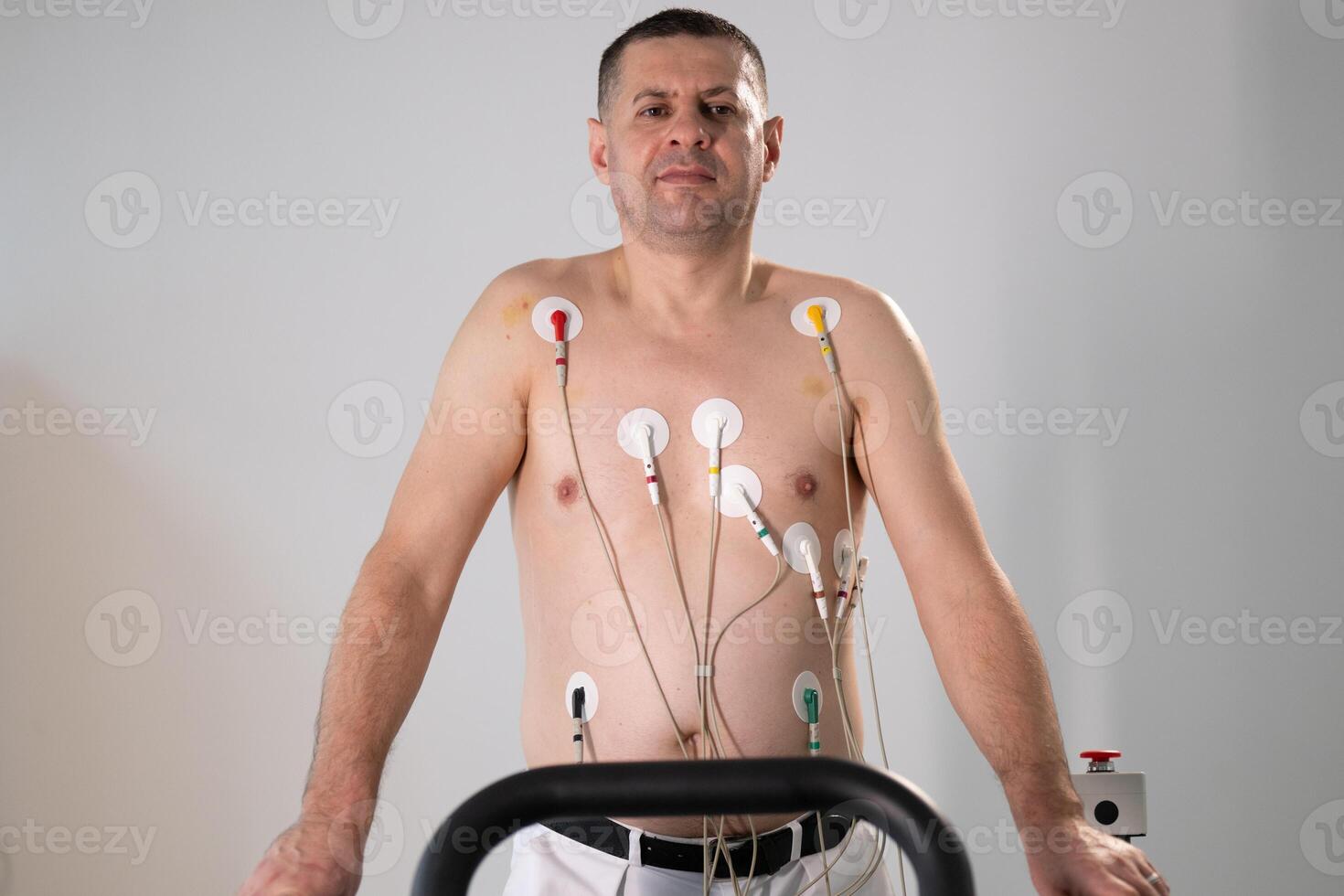 A middle-aged man is undergoing a medical stress test on a treadmill, connected to ECG electrodes for heart monitoring in a clinical environment photo