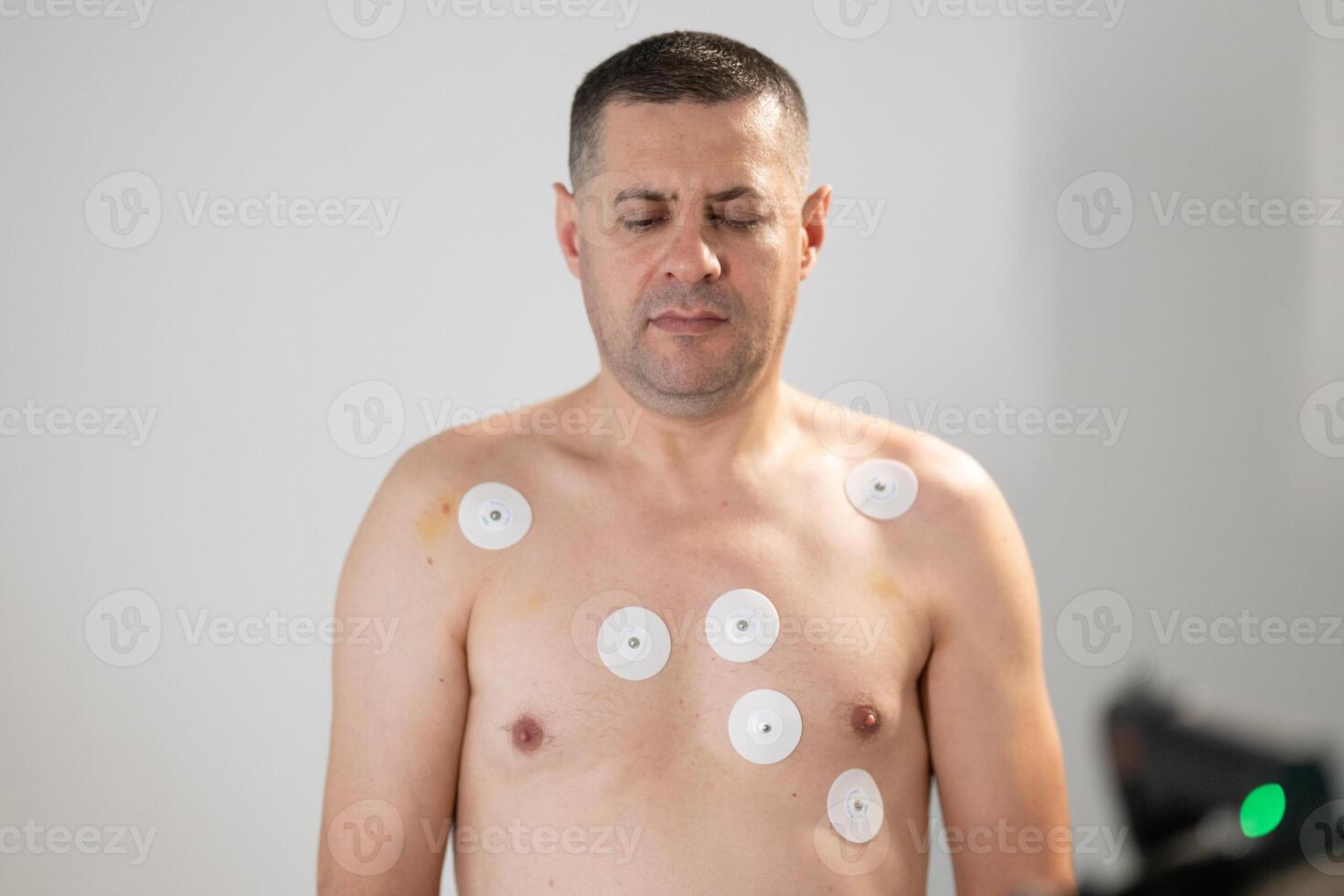 A middle-aged man is undergoing a medical stress test on a treadmill, connected to ECG electrodes for heart monitoring in a clinical environment photo