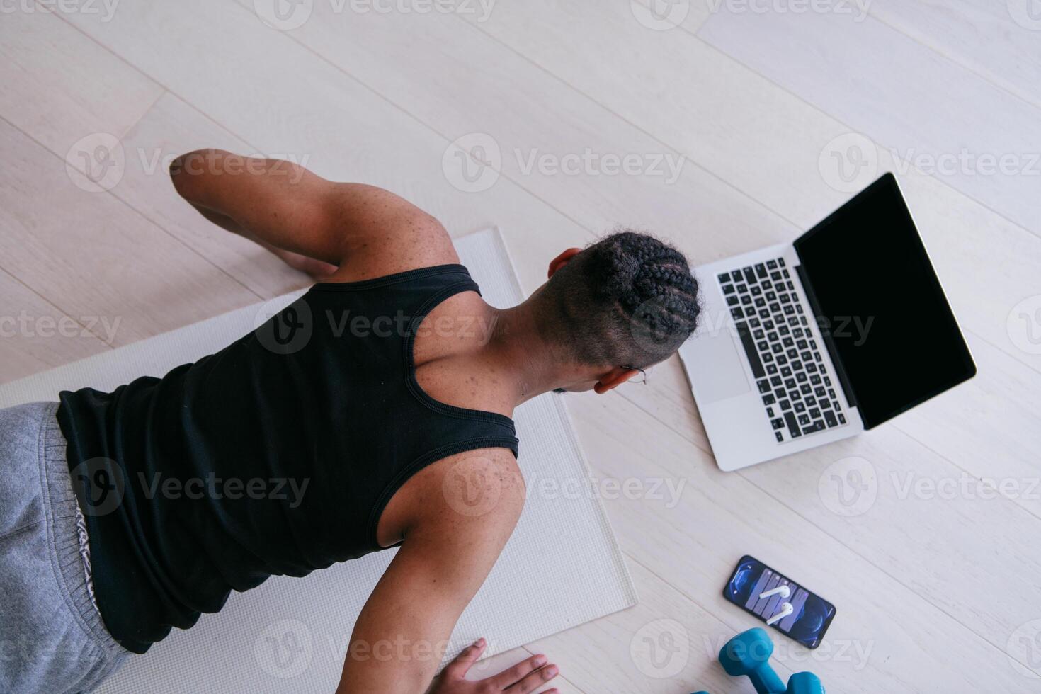 Training At Home. Sporty man doing the training while watching an online tutorial on a laptop, exercising in the living room, free space. photo
