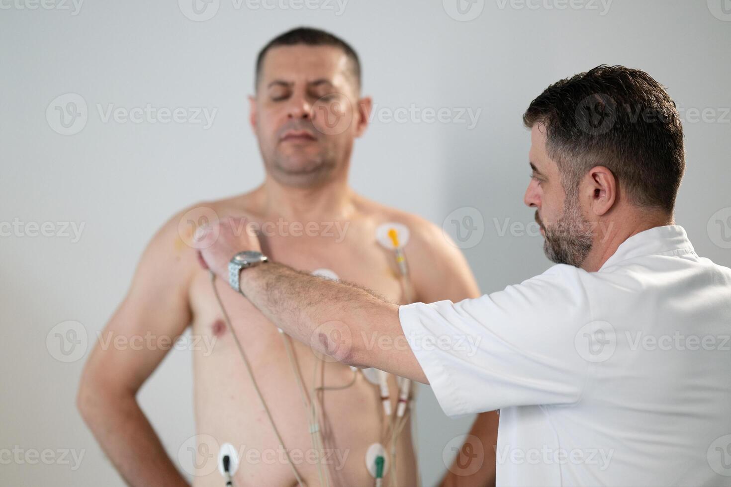 A middle-aged man is undergoing a medical stress test on a treadmill, connected to ECG electrodes for heart monitoring in a clinical environment photo