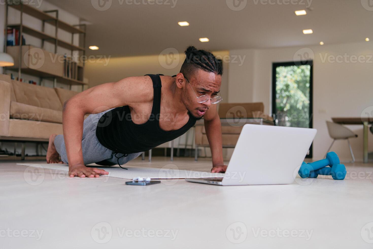 Training At Home. Sporty african american man doing the training while watching an online tutorial on a laptop, exercising in the living room, free space. photo