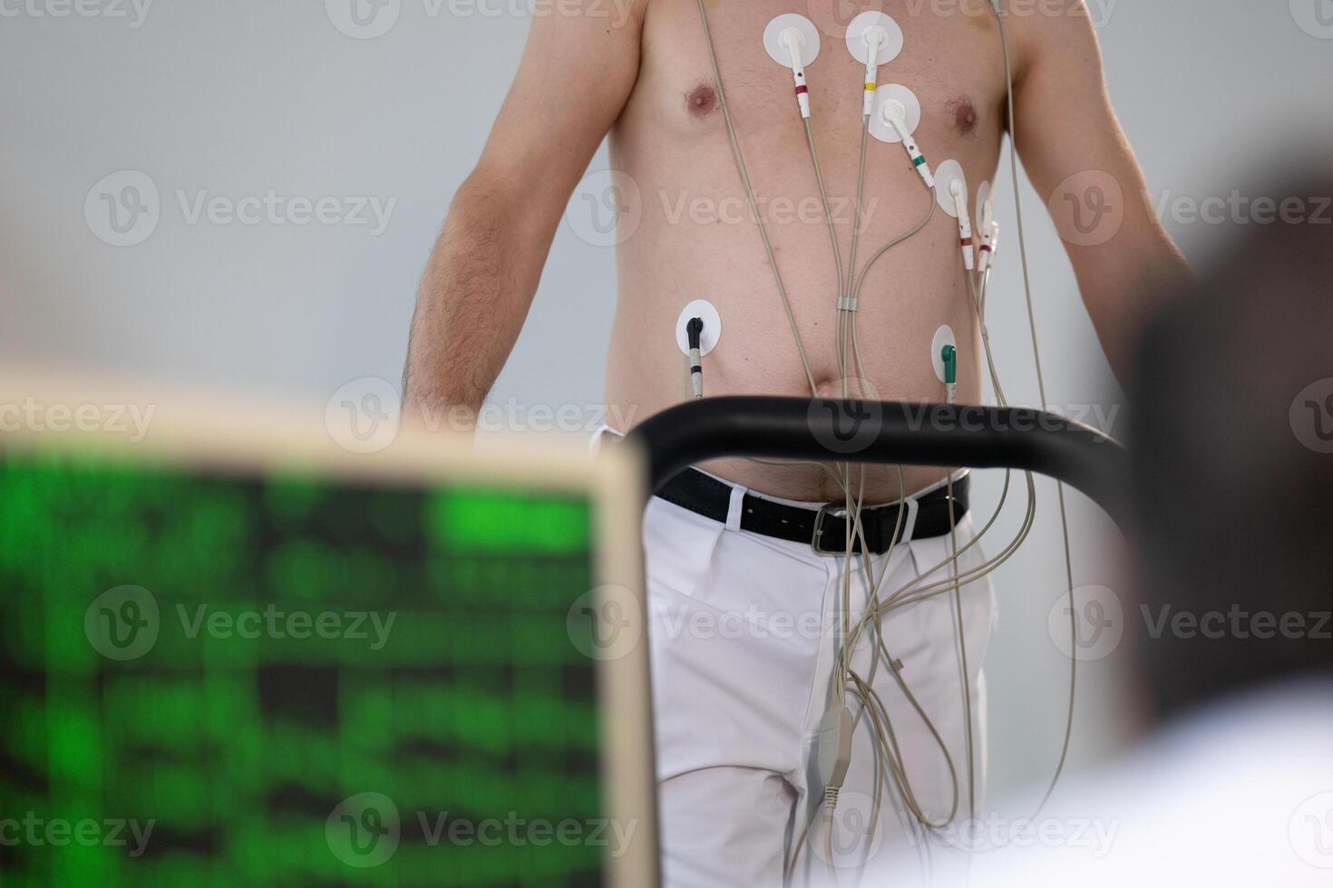 A middle-aged man is undergoing a medical stress test on a treadmill, connected to ECG electrodes for heart monitoring in a clinical environment photo