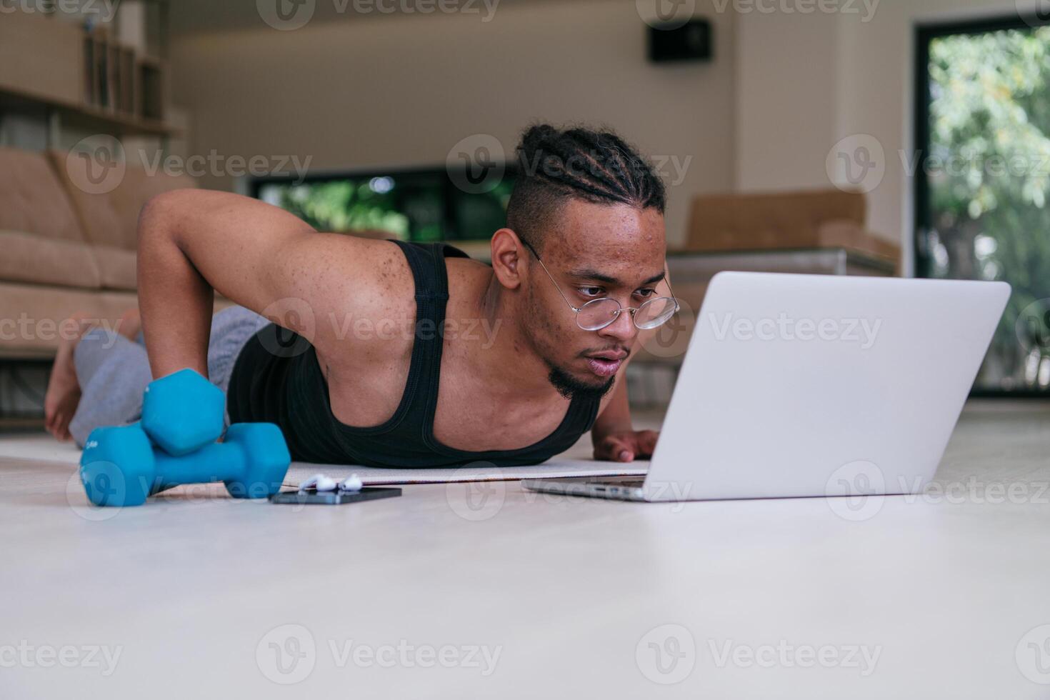Training At Home. Sporty african american man doing the training while watching an online tutorial on a laptop, exercising in the living room, free space. photo