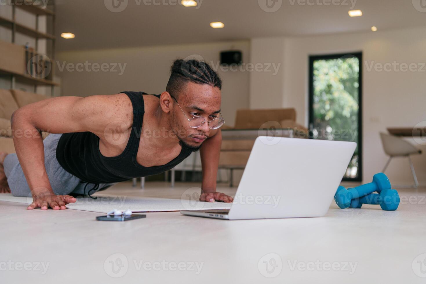 Training At Home. Sporty african american man doing the training while watching an online tutorial on a laptop, exercising in the living room, free space. photo