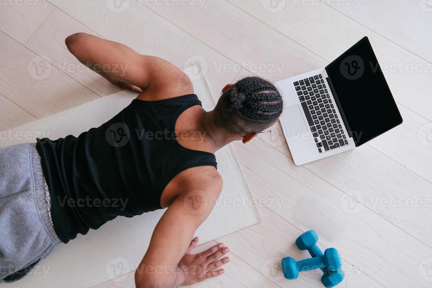 Training At Home. Sporty man doing the training while watching an online tutorial on a laptop, exercising in the living room, free space. photo