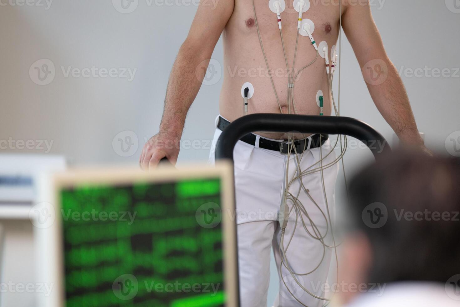 A middle-aged man is undergoing a medical stress test on a treadmill, connected to ECG electrodes for heart monitoring in a clinical environment photo