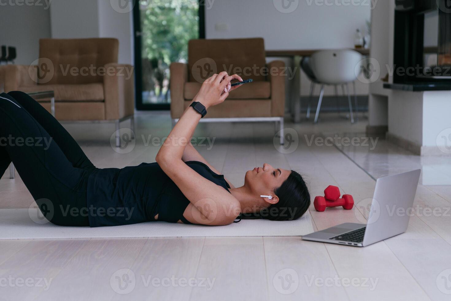 A sportswoman using a smartphone while resting and lying on the modern house floor photo