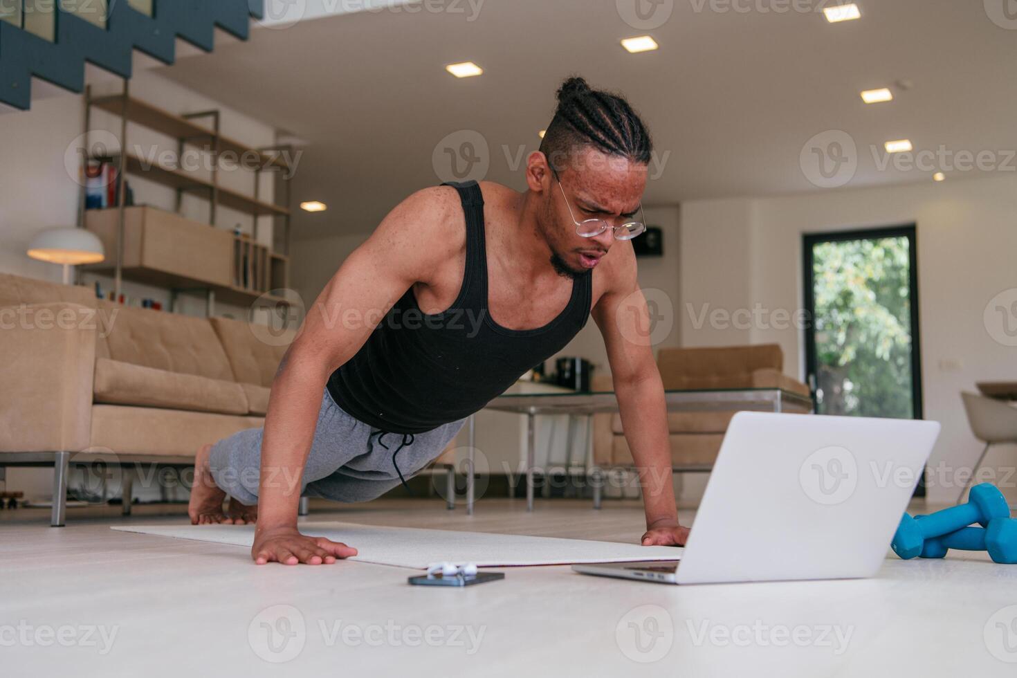 Training At Home. Sporty african american man doing the training while watching an online tutorial on a laptop, exercising in the living room, free space. photo