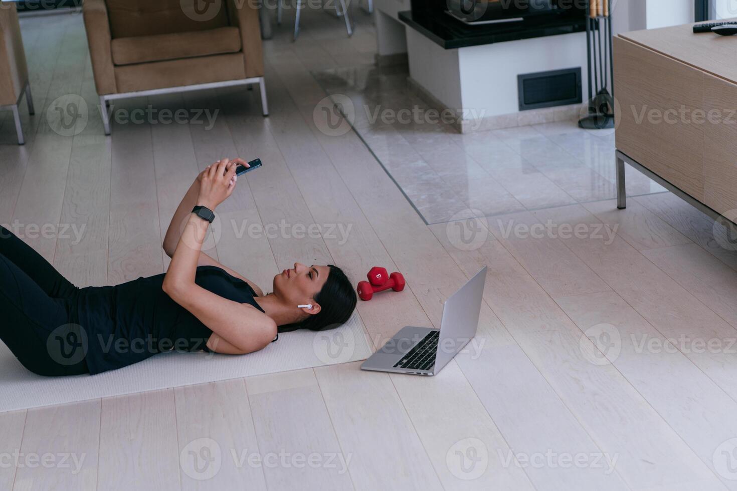 A sportswoman using a smartphone while resting and lying on the modern house floor photo