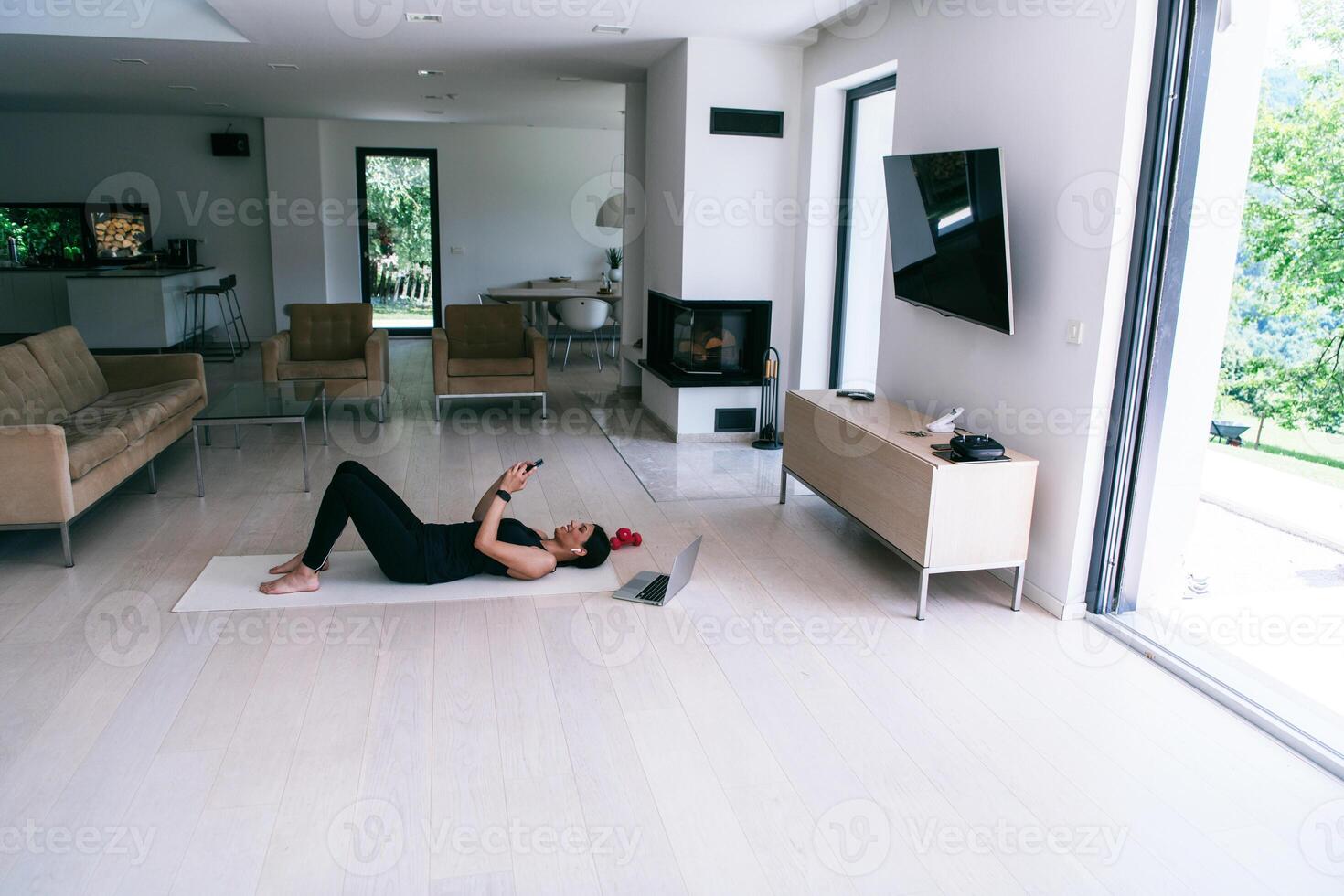 Sportswoman using a smartphone while resting and lying on the floor of modern house. photo