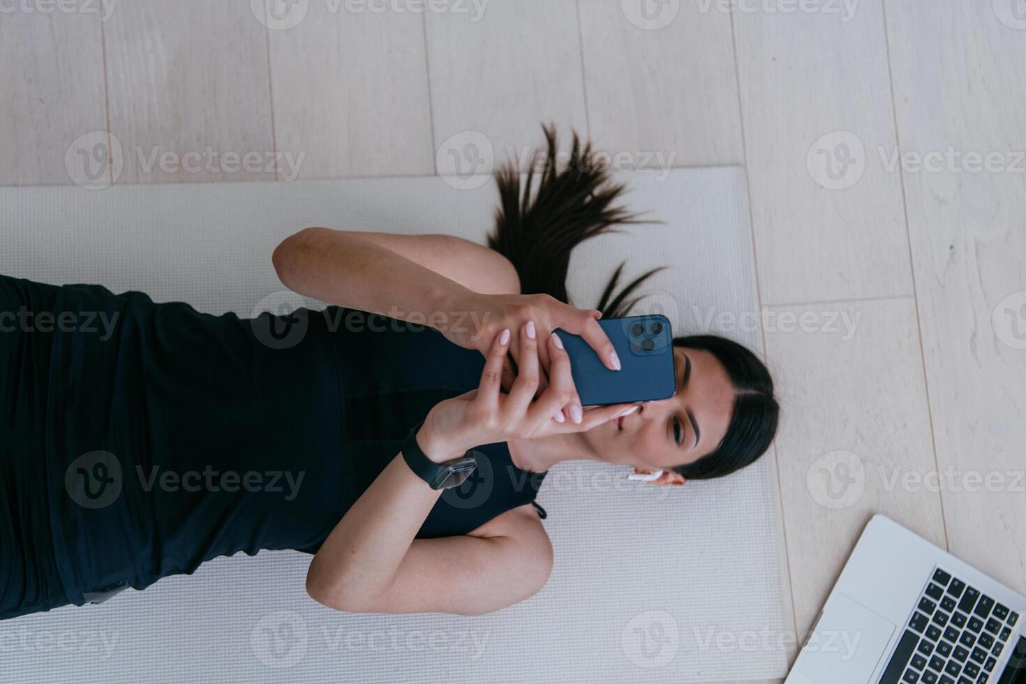 Sportswoman using a smartphone while resting and lying on the floor of modern house. photo
