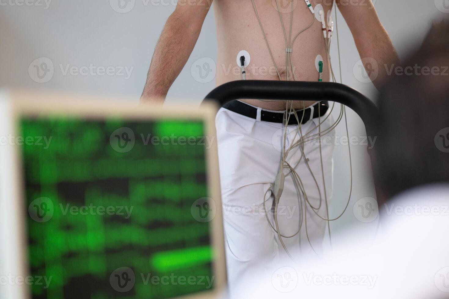 A middle-aged man is undergoing a medical stress test on a treadmill, connected to ECG electrodes for heart monitoring in a clinical environment photo