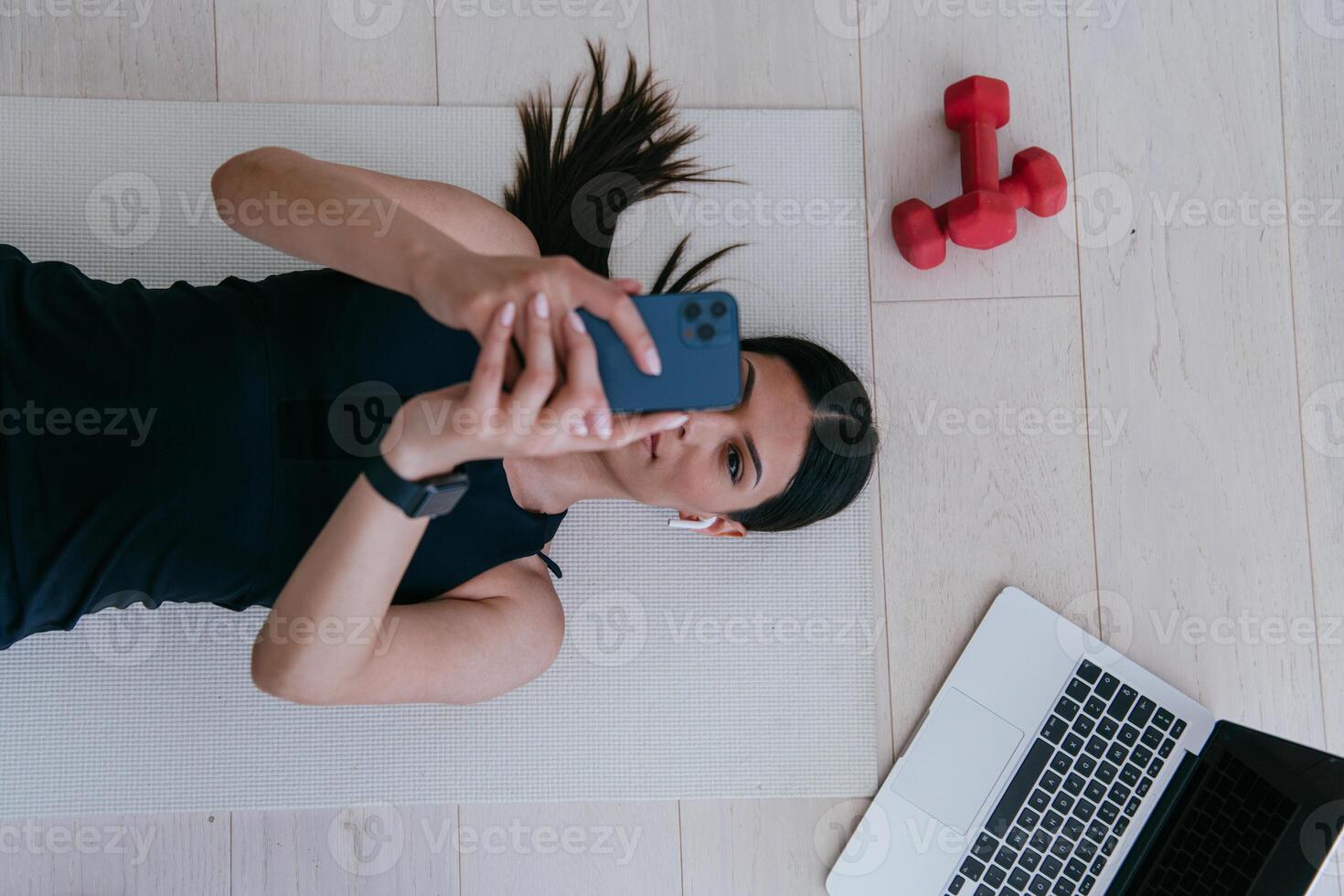 Sportswoman using a smartphone while resting and lying on the floor of modern house. photo