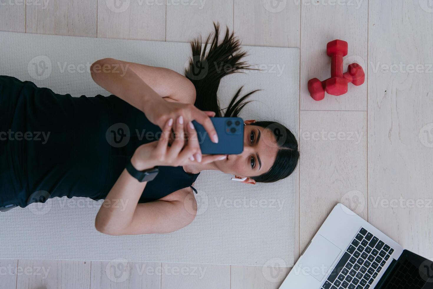 Sportswoman using a smartphone while resting and lying on the floor of modern house. photo
