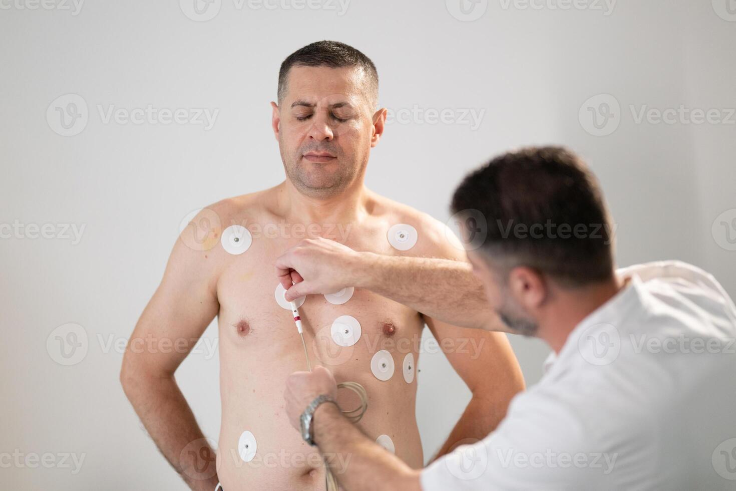 A middle-aged man is undergoing a medical stress test on a treadmill, connected to ECG electrodes for heart monitoring in a clinical environment photo