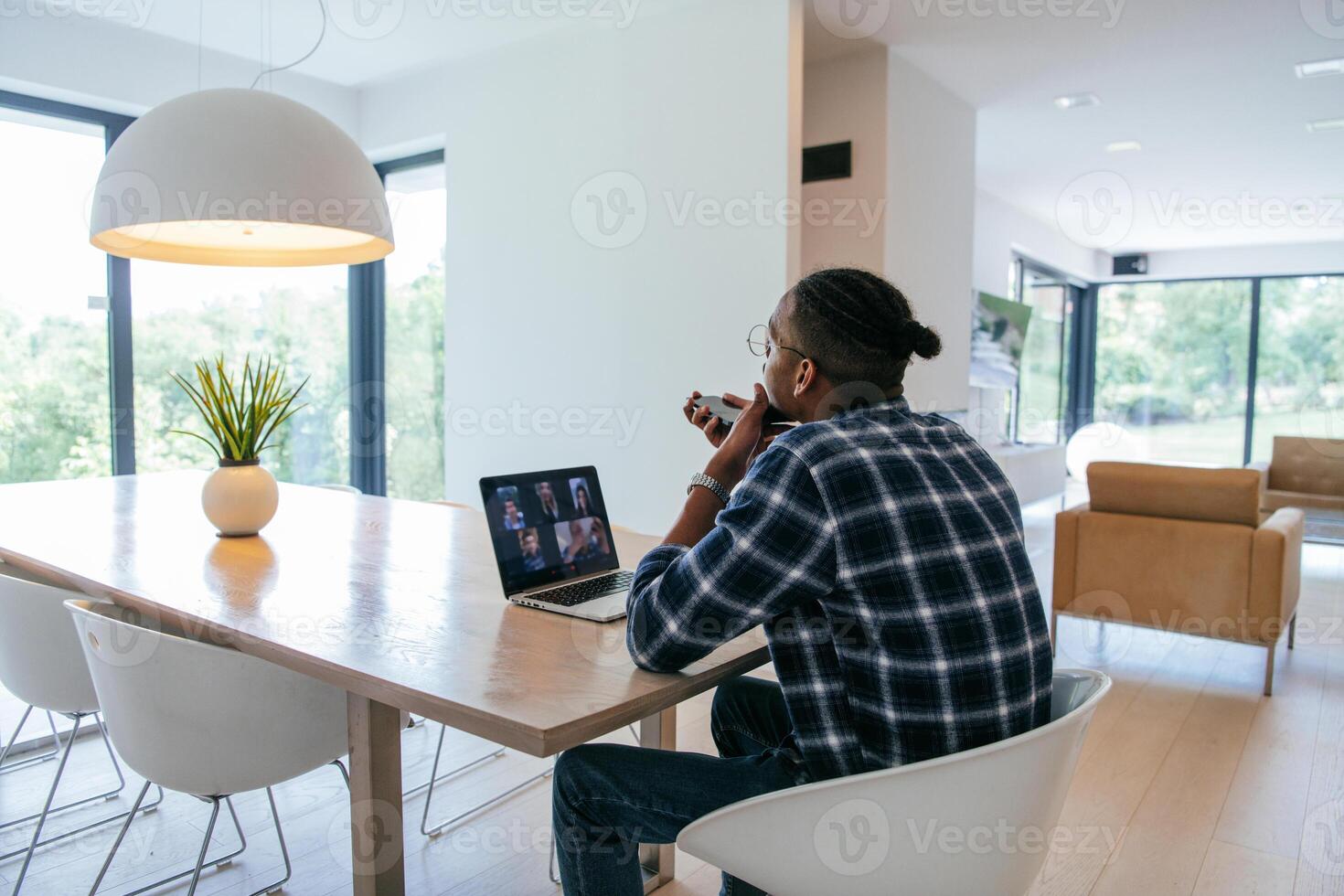 African American businessman in glasses sitting at a table in a modern living room, using a laptop and smartphone for business chat, conversation with friends and entertainment. photo
