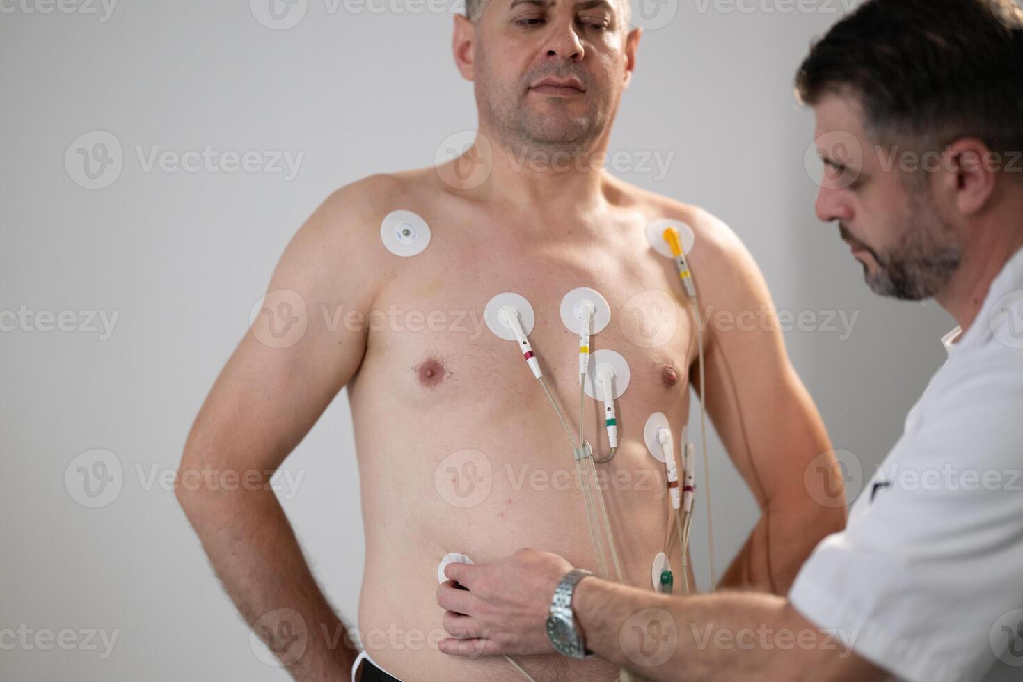 A middle-aged man is undergoing a medical stress test on a treadmill, connected to ECG electrodes for heart monitoring in a clinical environment photo