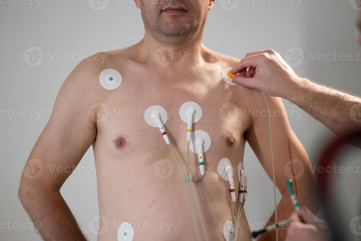 A middle-aged man is undergoing a medical stress test on a treadmill, connected to ECG electrodes for heart monitoring in a clinical environment photo