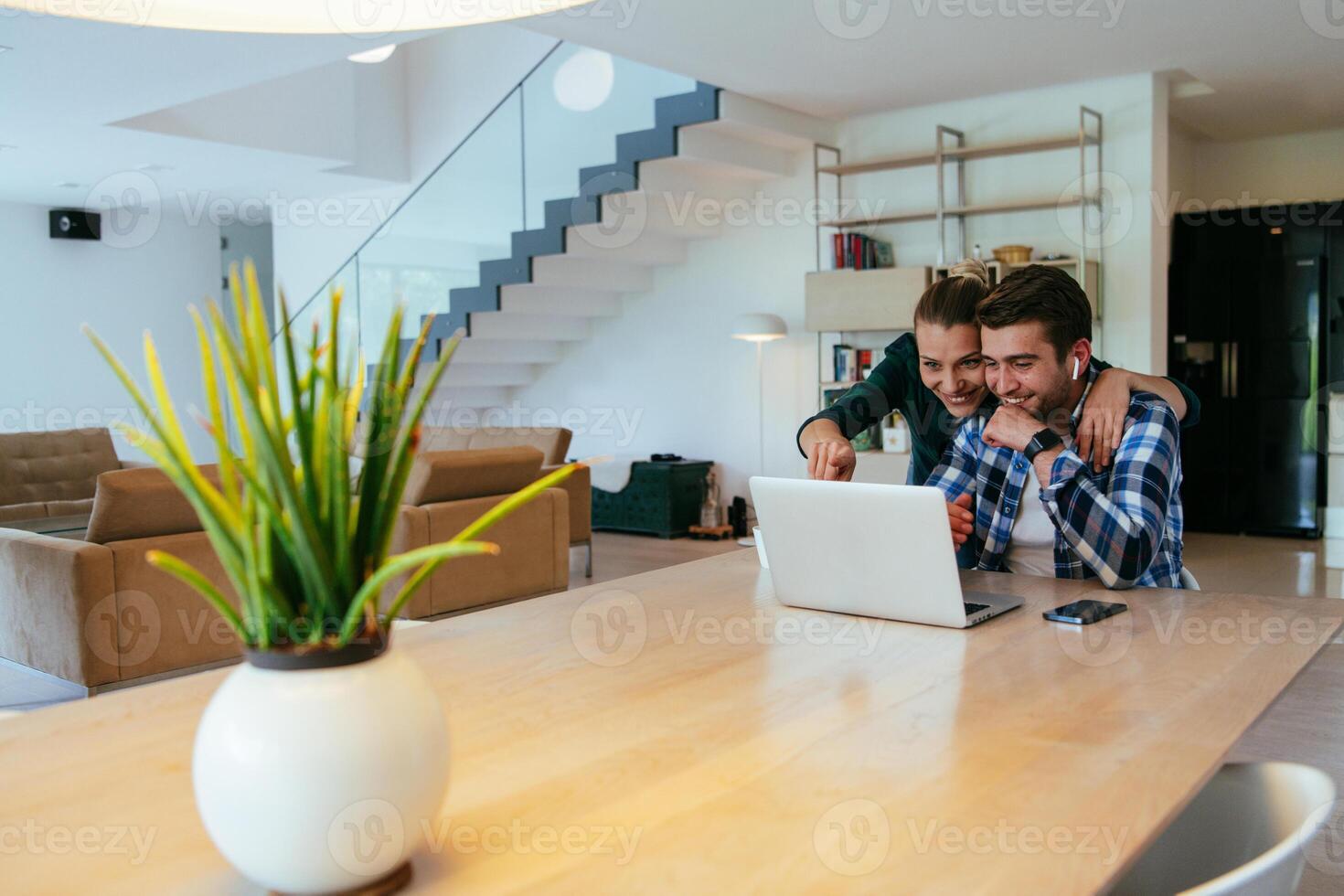 A young married couple is talking to parents, family and friends on a call via a laptop while sitting in the living room of their modern house. photo
