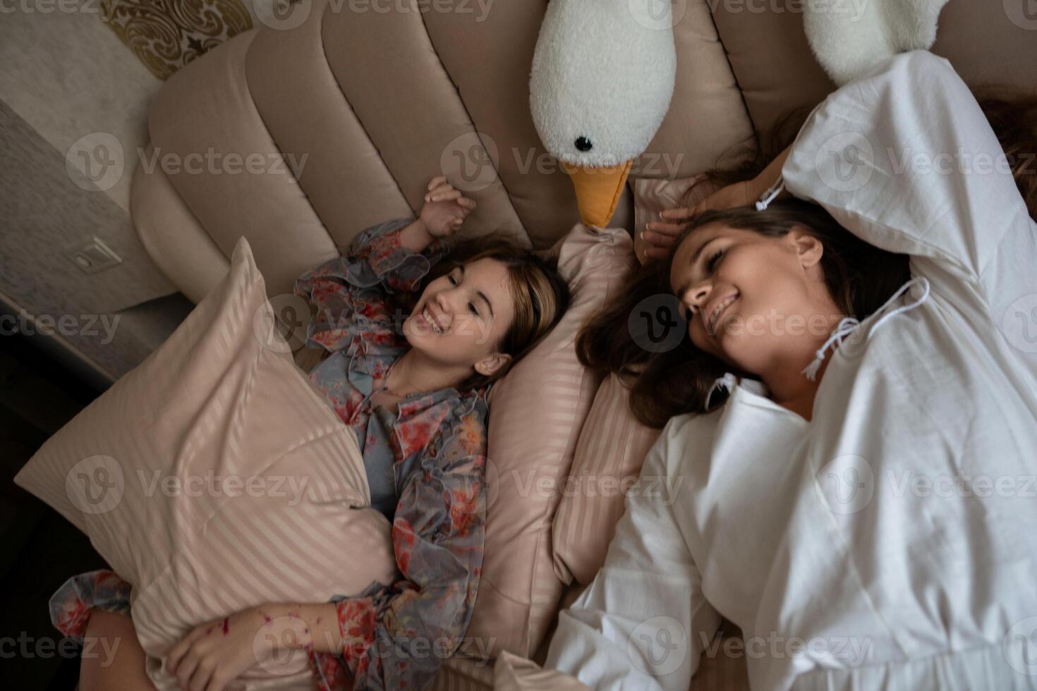 Women Girls Pillows. Indoor playful scene, two happy women and a girl relaxing on a bed with pillows and a swan toy, present day. photo