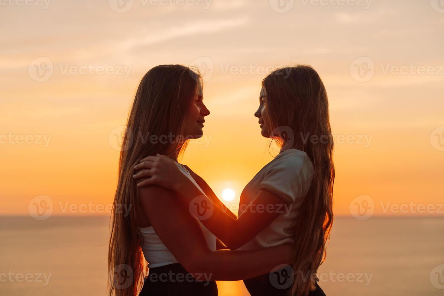 Mother daughter sunset. Mother and daughter stand on the beach, hugging and looking at each other enjoying the sunset. photo