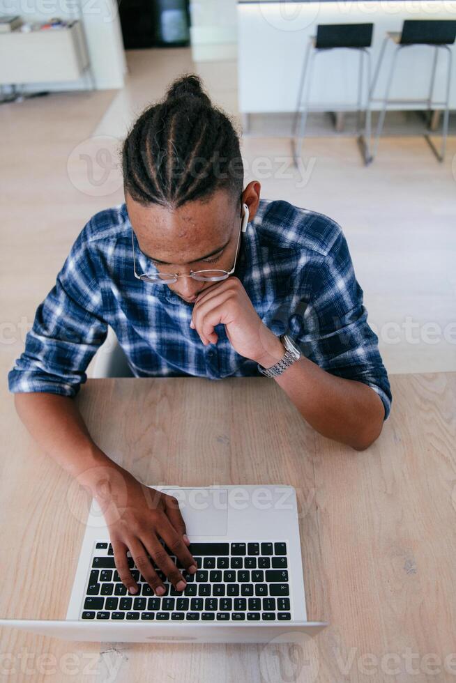 Top view of African American businessman in glasses sitting at a table in a modern living room, using a laptop and smartphone for business chat, conversation with friends and entertainment photo