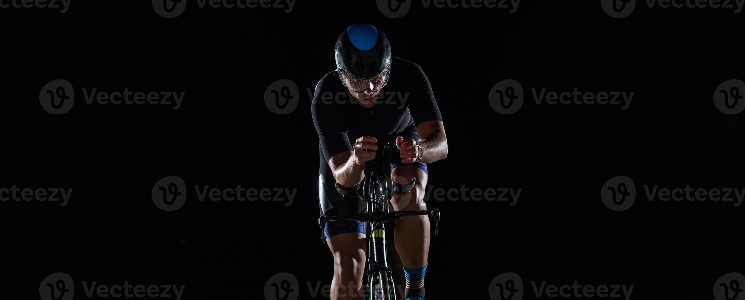 A triathlete rides his bike in the darkness of night, pushing himself to prepare for a marathon. The contrast between the darkness and the light of his bike creates a sense of drama and highlights the photo